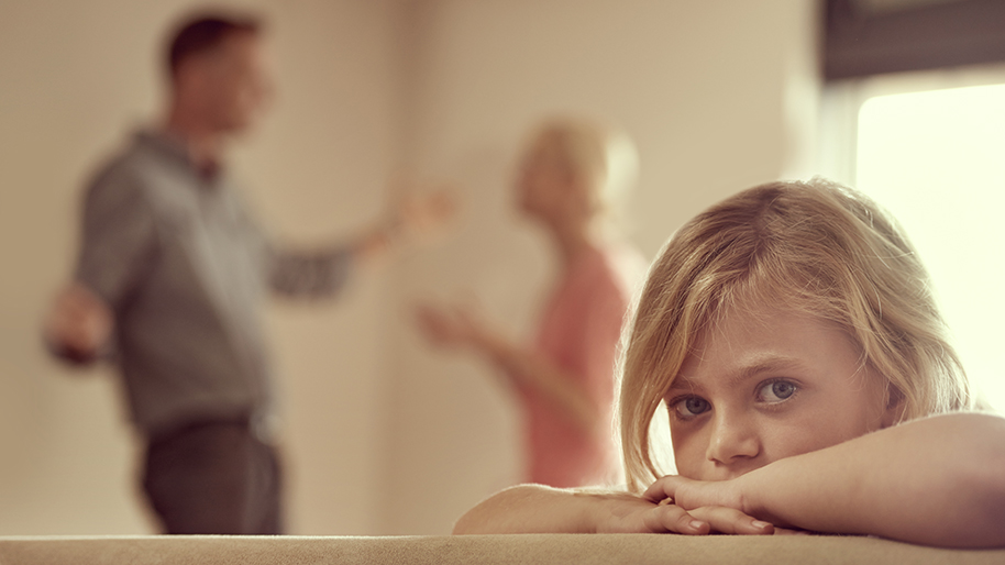 Little girl looking at the camera while her parents argue in the background