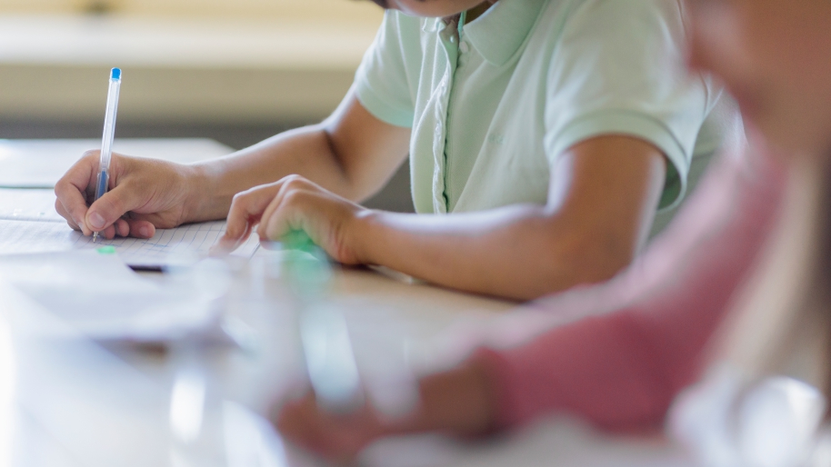Child writing on a piece of paper with a pencil