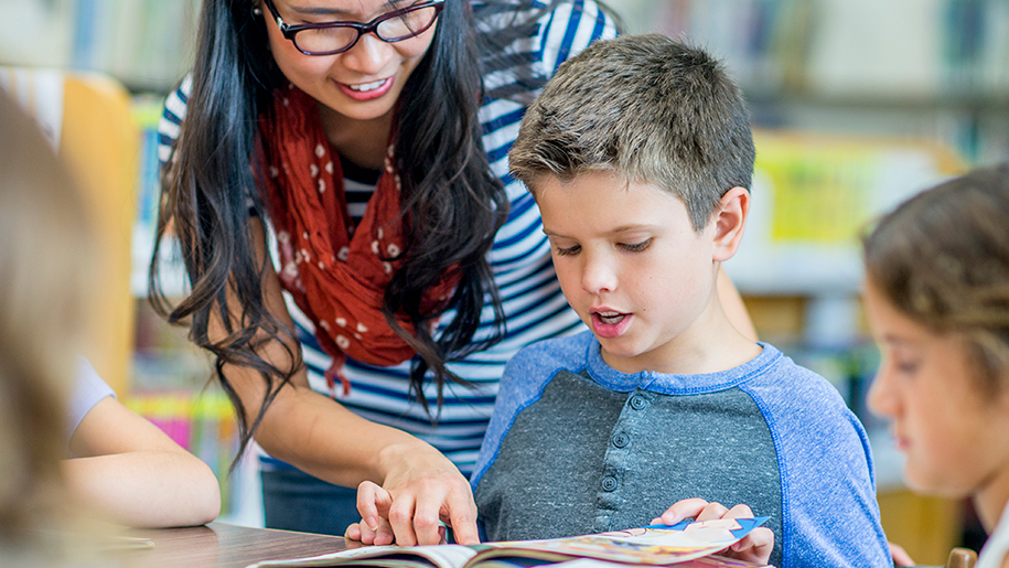 Little boy reading; teacher pointing at the text