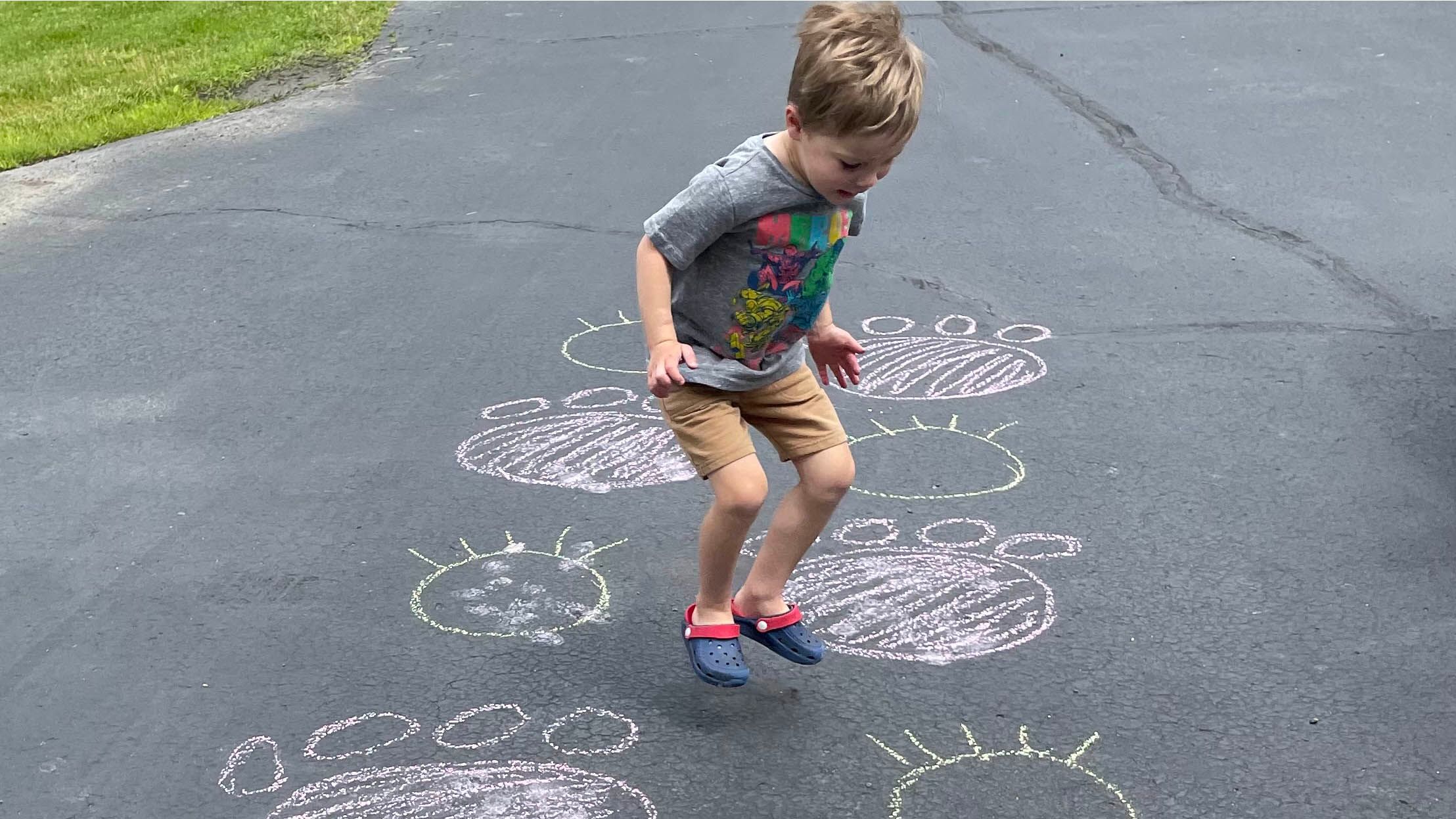 Child jumping on cement surrounded by chalk animal tracks drawings