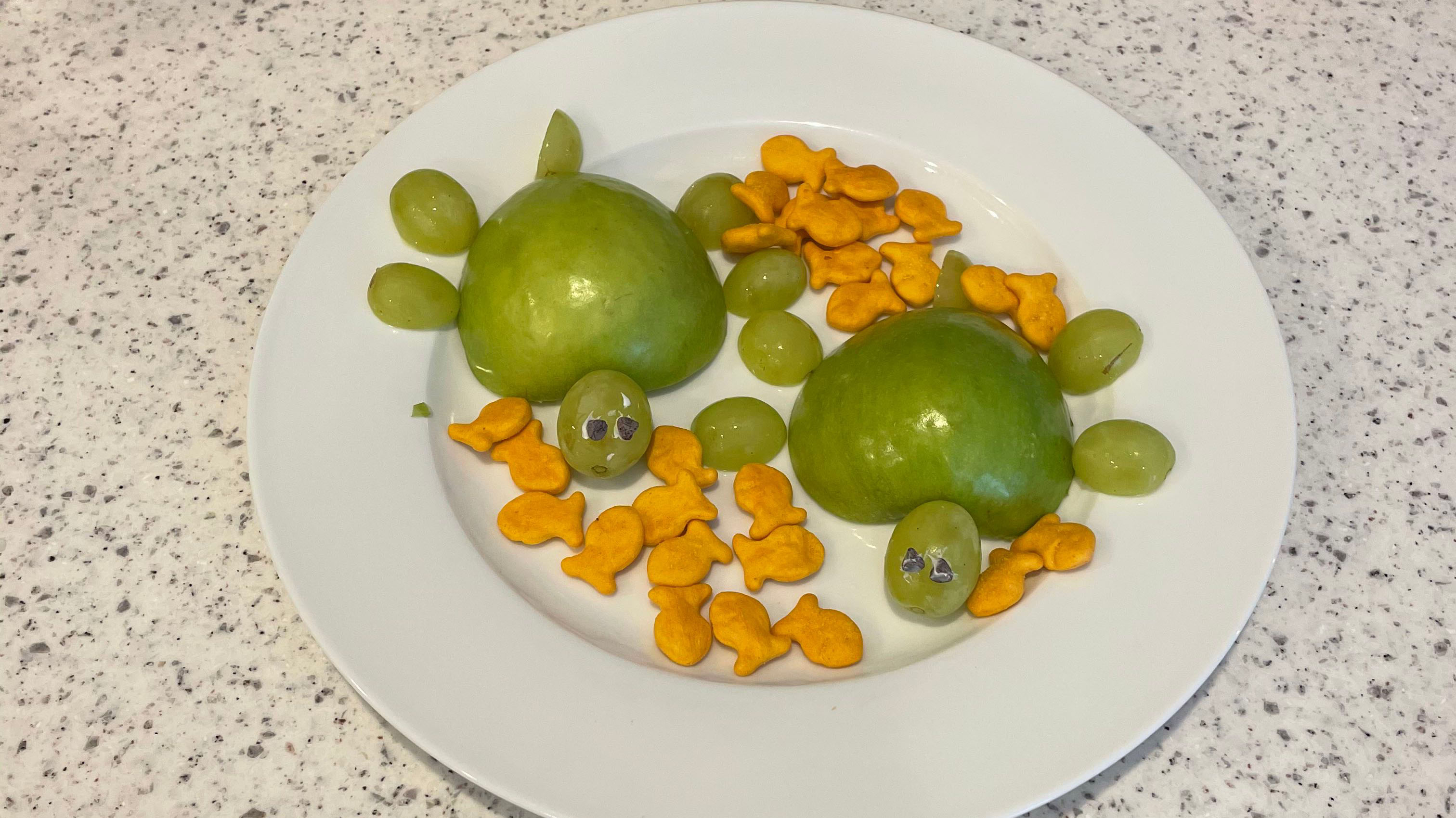 Orange fishy crackers on plate with green apples cut out in the shape of a turtle