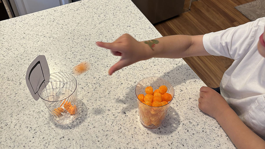 Child tossing a cheeto into a plastic cup resembling a basketball net and hoop