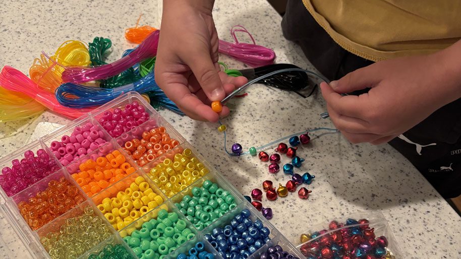 C.hild putting assortment of colorful beads on colorful string to make bracelet.
