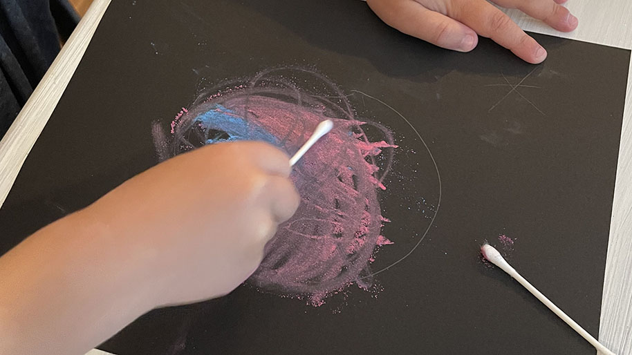 Child drawing out the shape of your galaxy using the pencil on the black paper.
