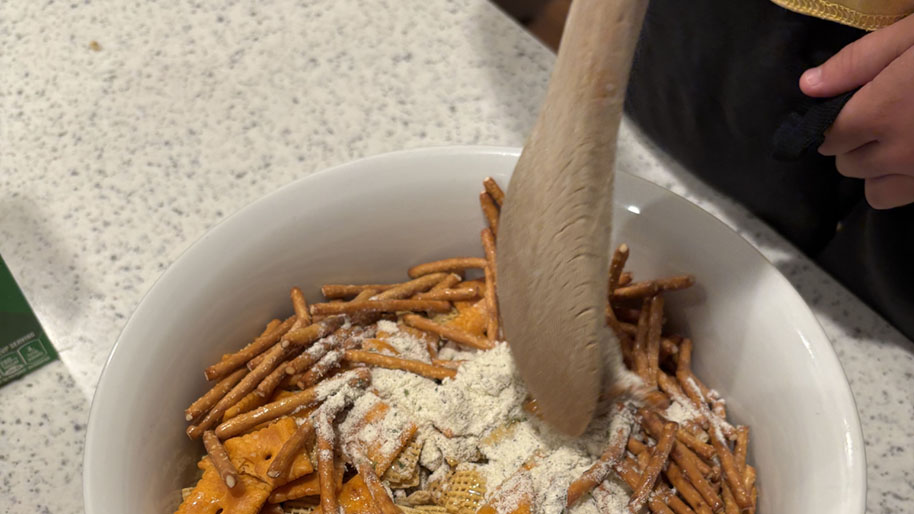 Chex mix in a bowl with seasoning and spoon for stirring