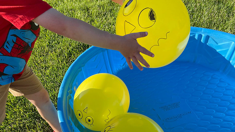 Child placing yellow balloons with face drawings on them in blue pool
