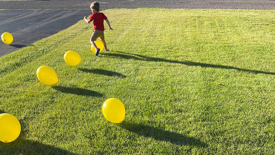 Child chasing and kicking yellow ballons in yard