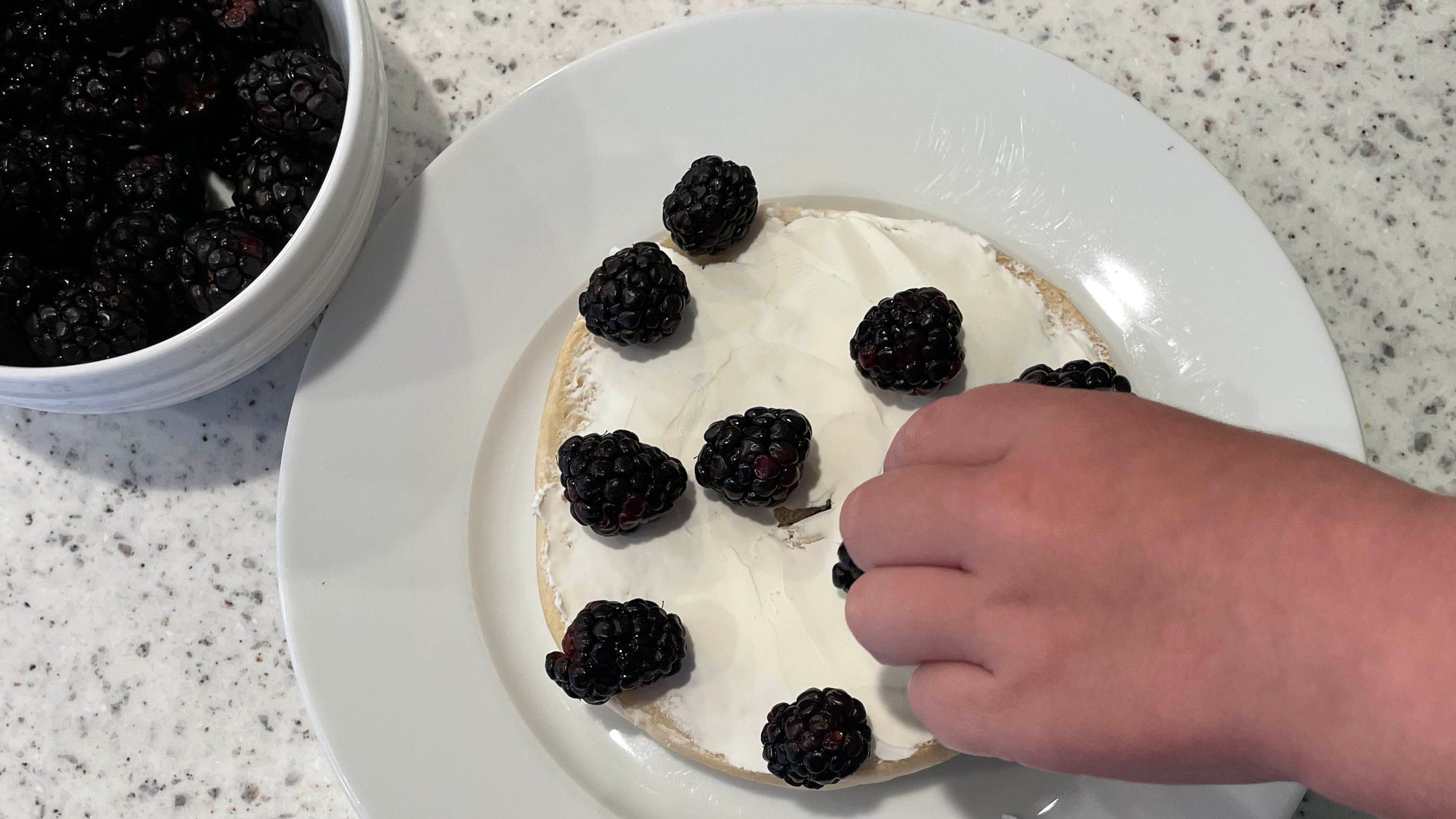 Childs hand placing raspberries on top of cream cheese bagel