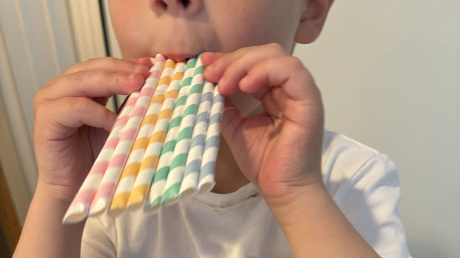 Child holding and blowing through colorful straws for flute project.