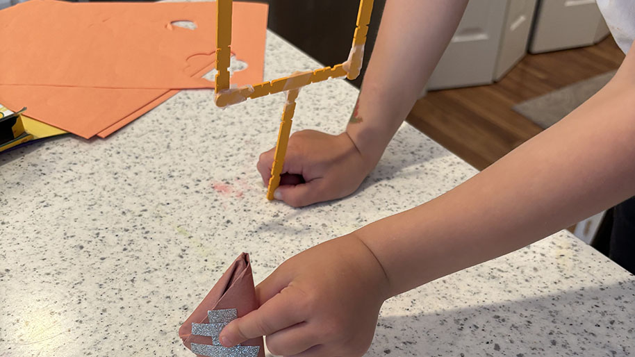 Child holding paper football and goal post made of popsicle sticks