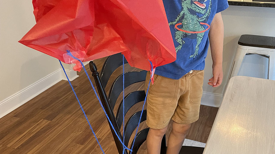 Child holding red tissue paper attached to blue yard