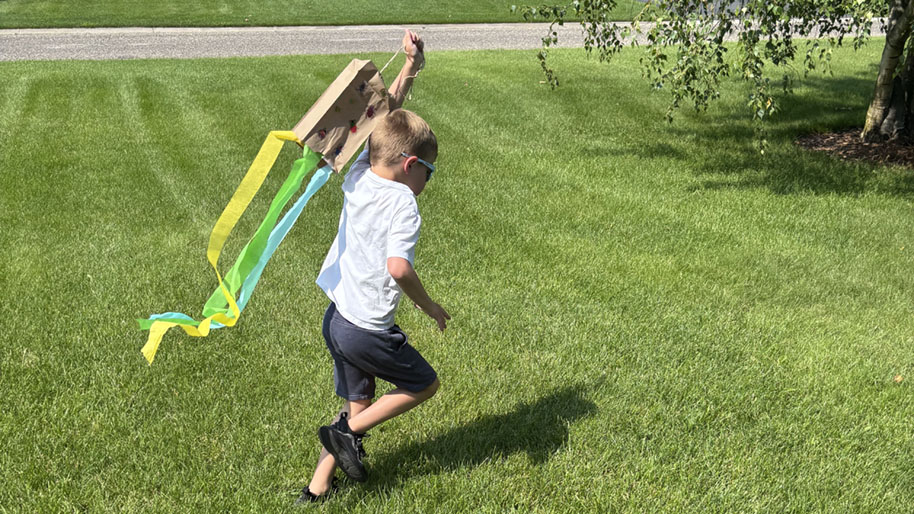 Child running with paper bag kite with colorful tissue streamers