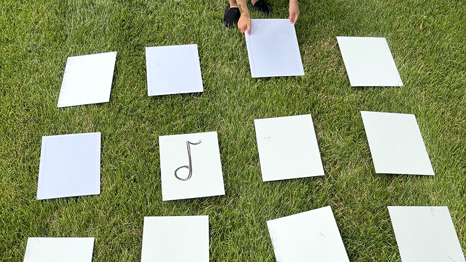 Child placing music note cards in rows on the grass