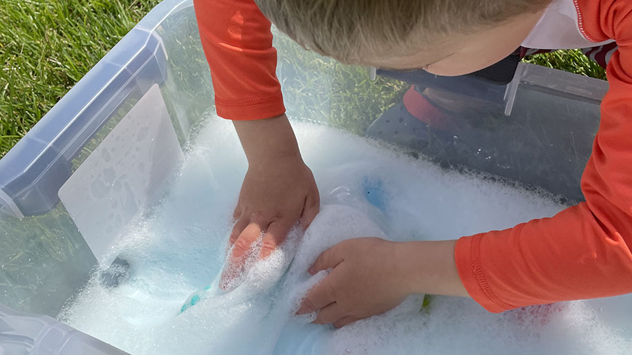 Child in an orange shirt playing in ocean foam