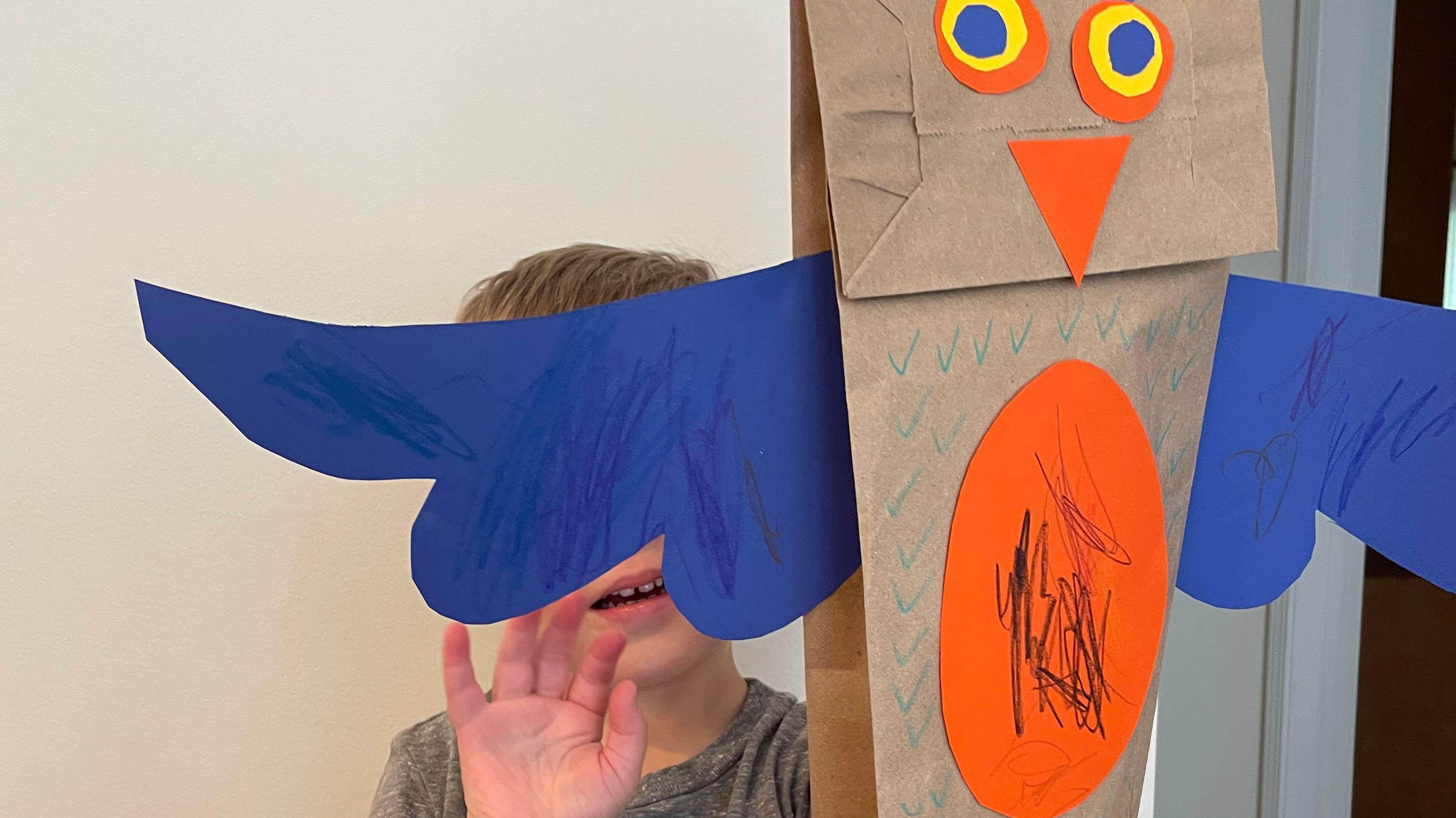 Child holding up owl puppet with colored cutouts attached