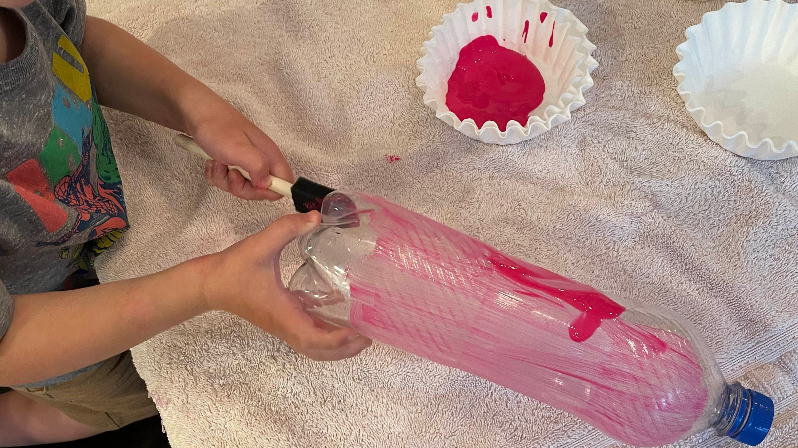 Child holding and painting plastic bottle pink with form brush