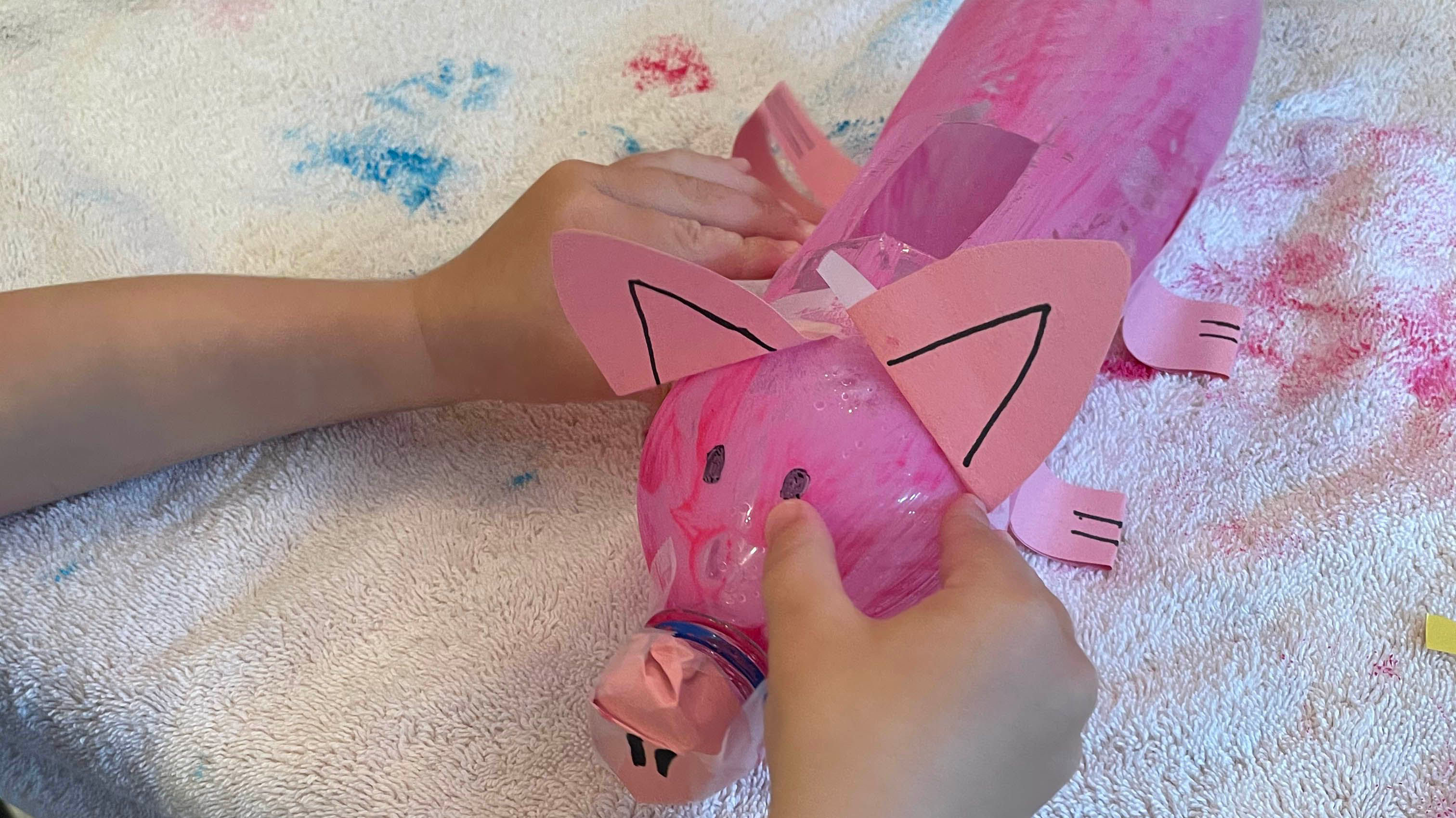 Child adding paper cut out ears to pink piggy bank