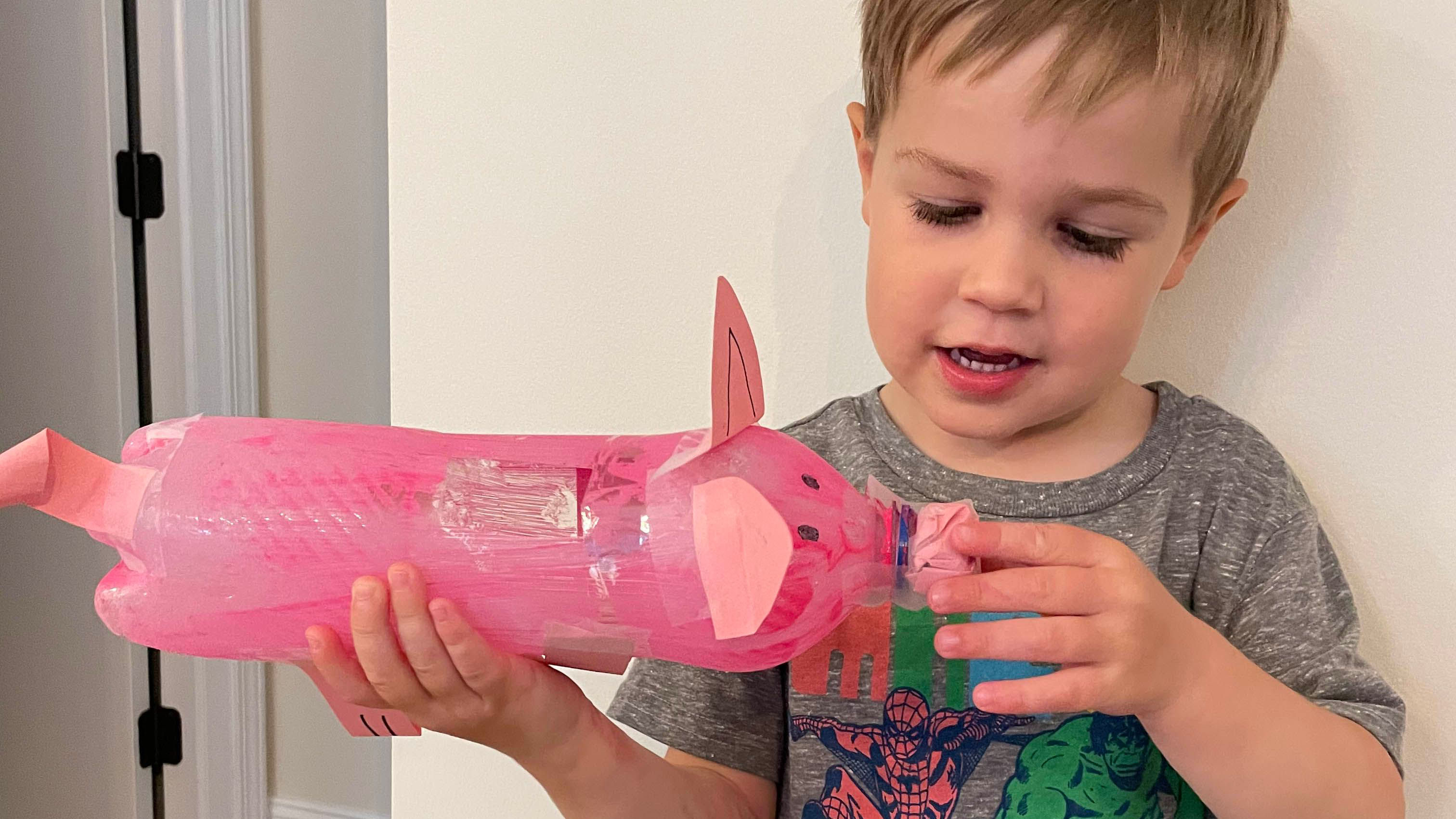 Child smiling holding plastic bottle painted and decorated as a pig