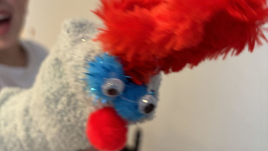 Child holding colorful hand puppet that they made with sock, eyes and feathers.