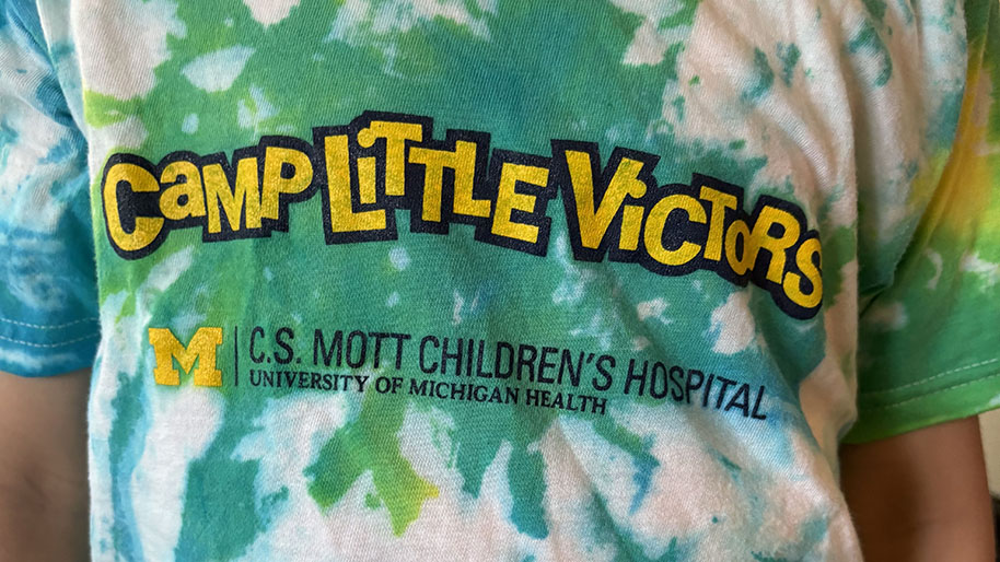 Child wearing colorful tie-dyed shirt reading Camp Little victors.