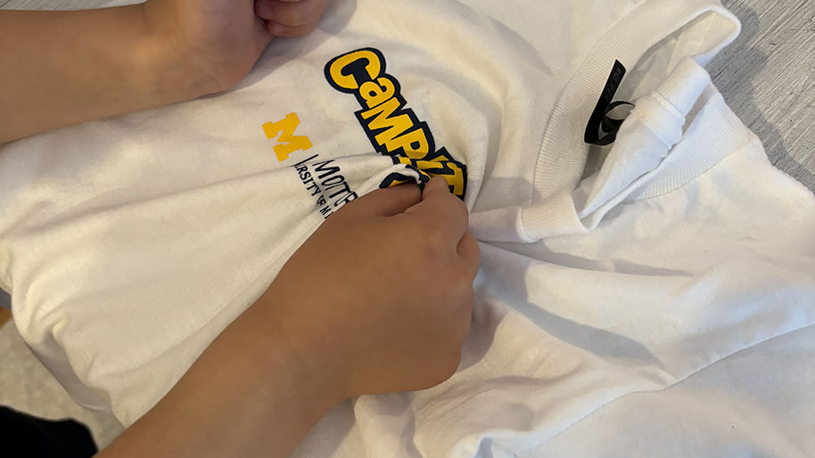 Child placing a rubber band around the circular, rolled up shirt in a vertical direction and the other rubber band around the shirt in a horizontal direction.