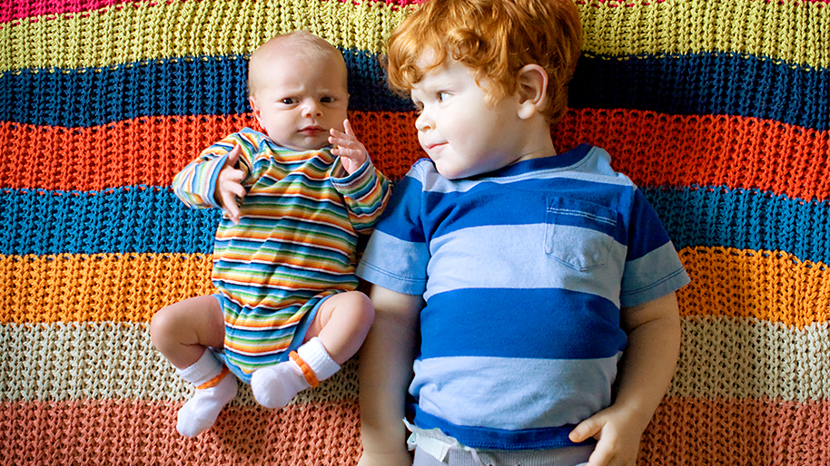Toddler boy laying next to a baby