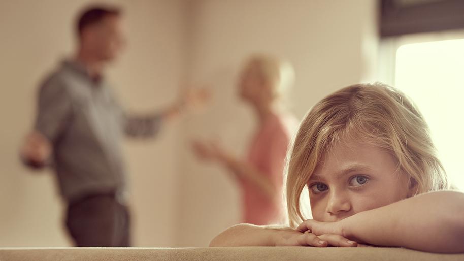 Little girl looking at the camera while her parents argue in the background