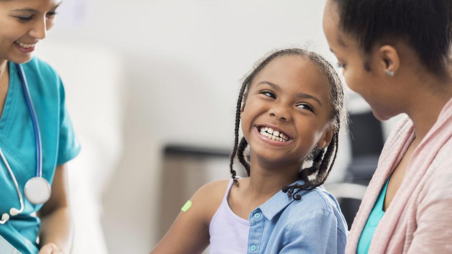 Young girl with a bright green bandaid on her upper arm, smiling up at her mother 