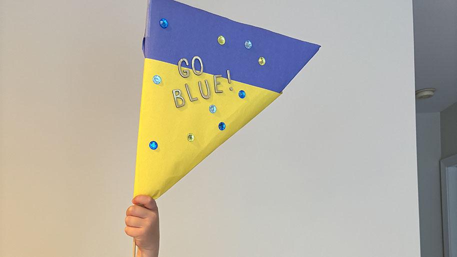 Child holding yellow and blue pennant in the air decorated