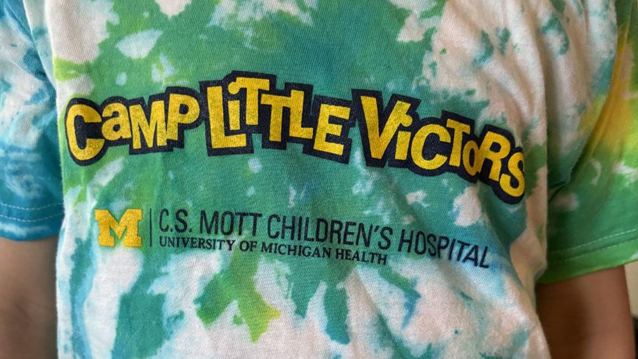 Child wearing colorful tie-dyed shirt reading Camp Little victors.