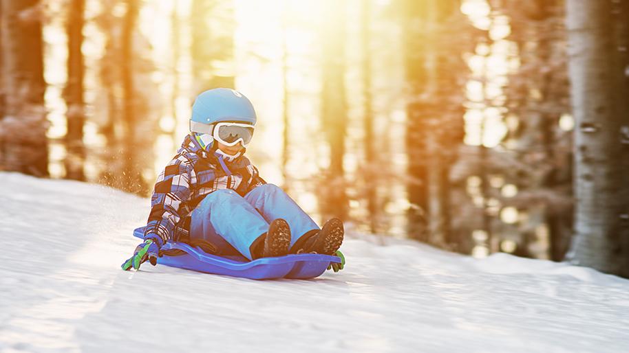 Child sledding down a hill with trees in background