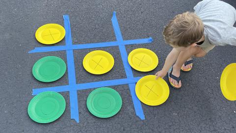 Child placing colored paper plates on the 3 x 3 painters tape grid for tic tac toe game