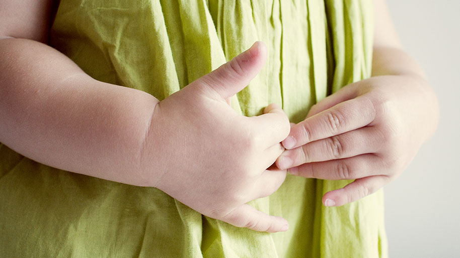Child's hands rubbing her stomach over a green top