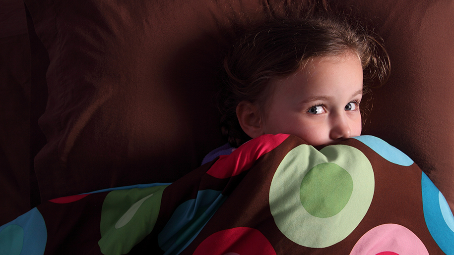 Little girl peeking out from under the covers